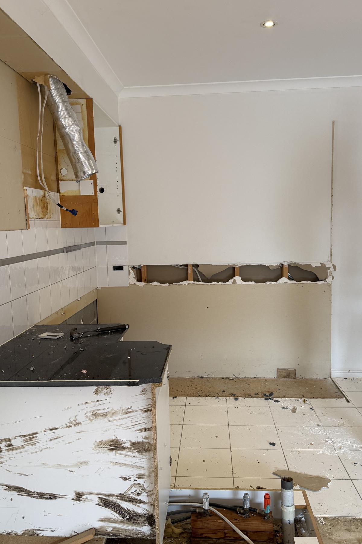 Stripped kitchen with the benchtop broken up and plumbing exposed through the floor.