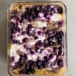 Overhead view of lemon blueberry baked oats with swirls of yogurt and juicy blueberries in a glass baking dish.