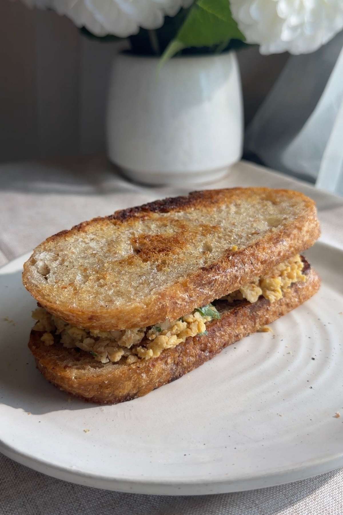 Mashed chickpea sandwich served on a white plate.
