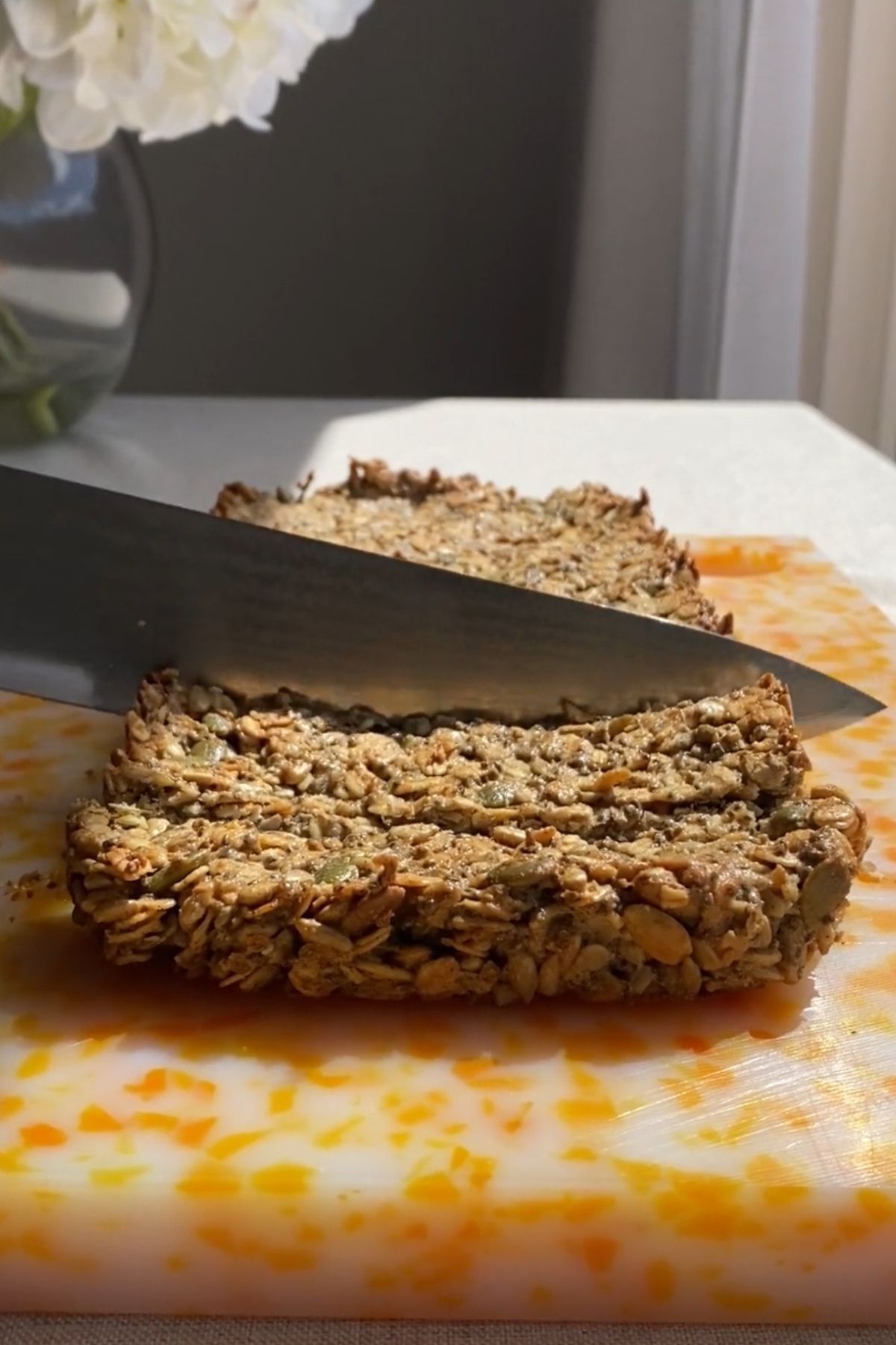Nut-free granola bars on a cutting board, with a knife slicing one bar into rectangles.