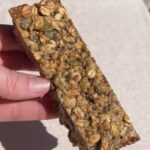 Close-up of a chewy nut-free granola bar held by hand, showing the oat and seed texture.