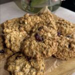 Pile of oatmeal cookies with dried cranberries on parchment and a wooden board.