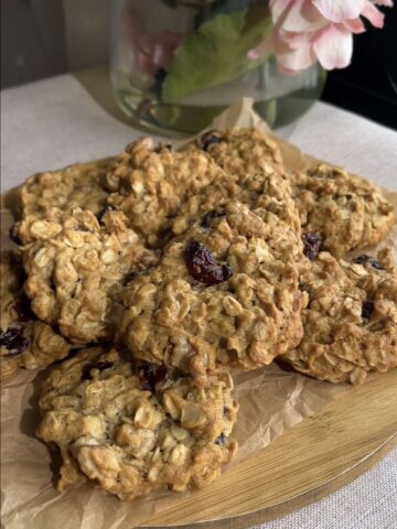 Pile of oatmeal cookies with dried cranberries on parchment and a wooden board.