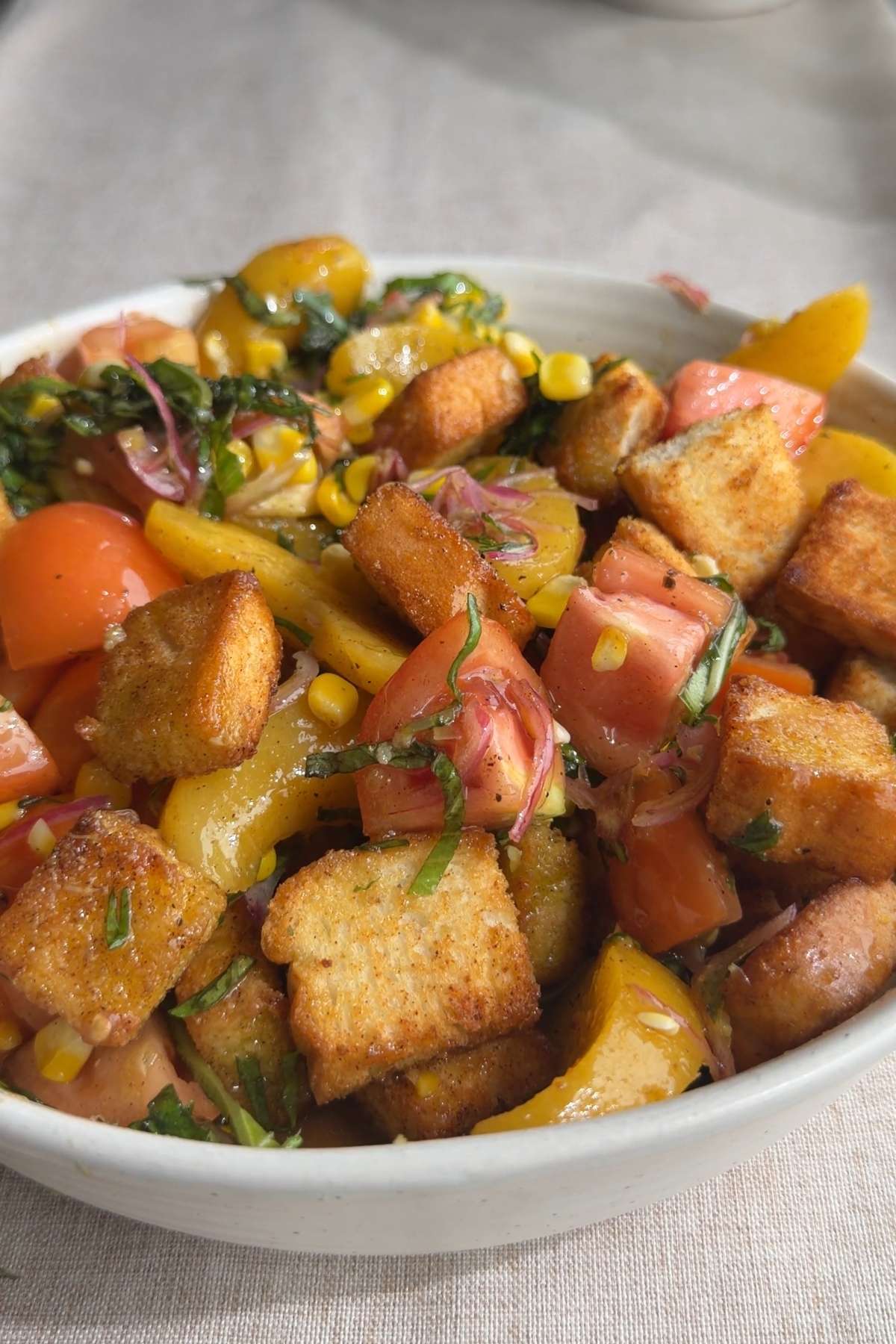 Close-up of peach panzella salad with croutons, tomatoes, corn, and basil.