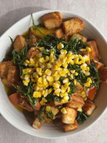 Overhead view of peach panzella salad topped with basil, corn, and croutons.