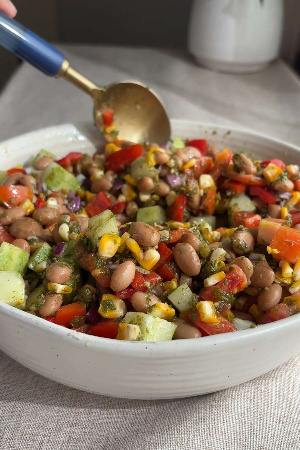 Spoon stirring pinto bean salad with corn, tomatoes, cucumber, and pinto beans.