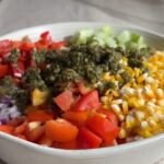 Bowl of chopped vegetables, corn, pinto beans, and herb dressing before mixing.