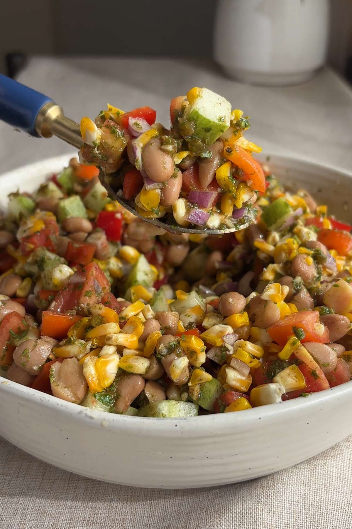 Spoon lifting pinto bean salad with corn, cucumber, tomatoes, and red onion.