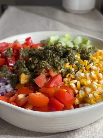 Bowl of chopped vegetables, corn, pinto beans, and herb dressing before mixing.