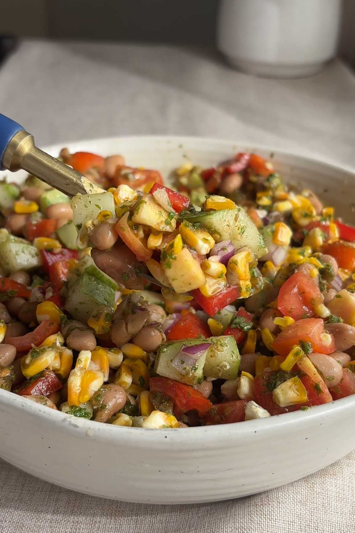 Spoon lifting pinto bean salad with corn, cucumber, tomatoes, and red bell pepper.