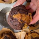 Hand holding a pumpkin chocolate swirl muffin with a marbled chocolate top.