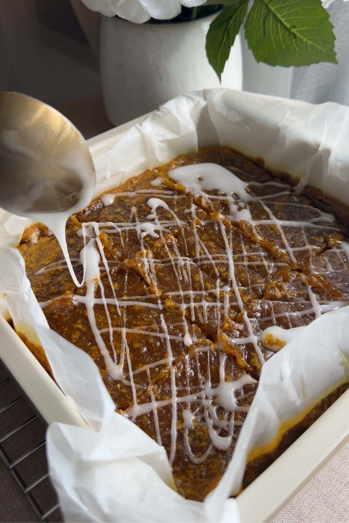 Glaze being drizzled over freshly baked pumpkin pie bars in the pan.