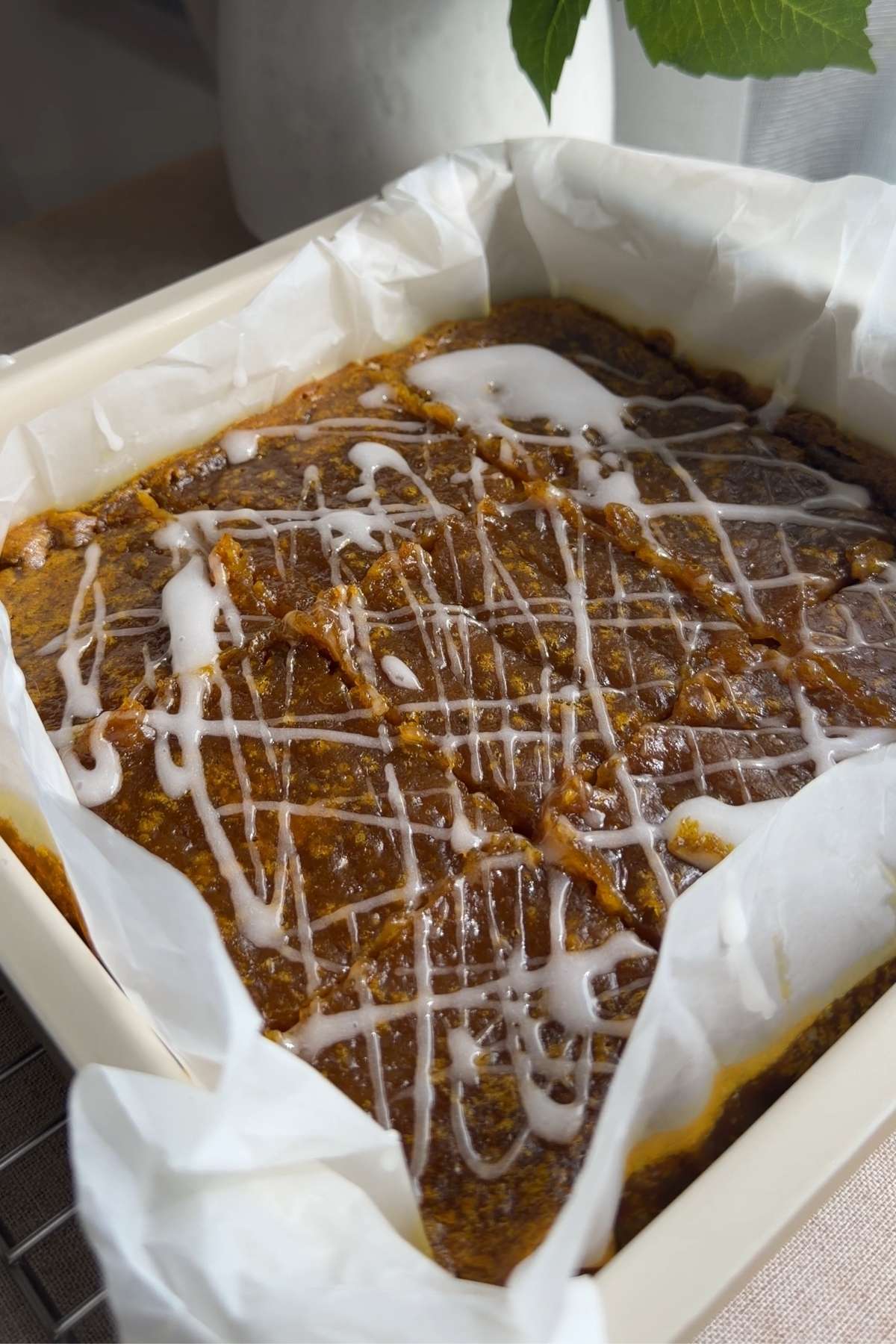 Pumpkin pie bars in a parchment-lined pan drizzled with a simple white glaze.