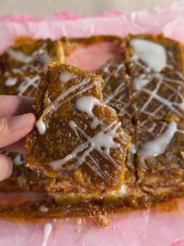 Hand holding a pumpkin pie bar with creamy pumpkin filling and white glaze.