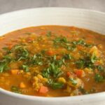 Close-up of red lentil coconut soup garnished with chopped cilantro in a white bowl.