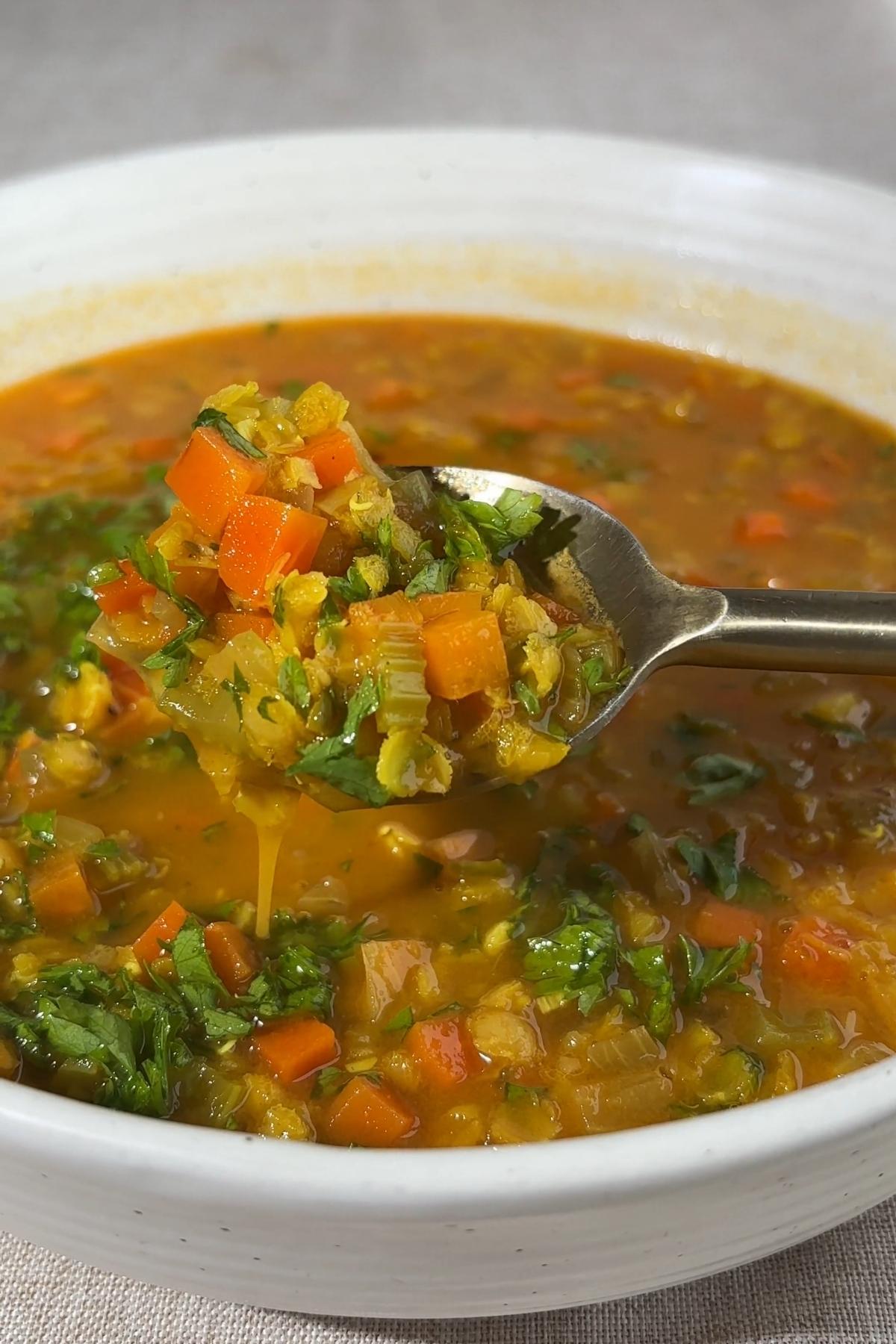 Spoon lifting red lentil soup with carrots, celery, and chopped cilantro.