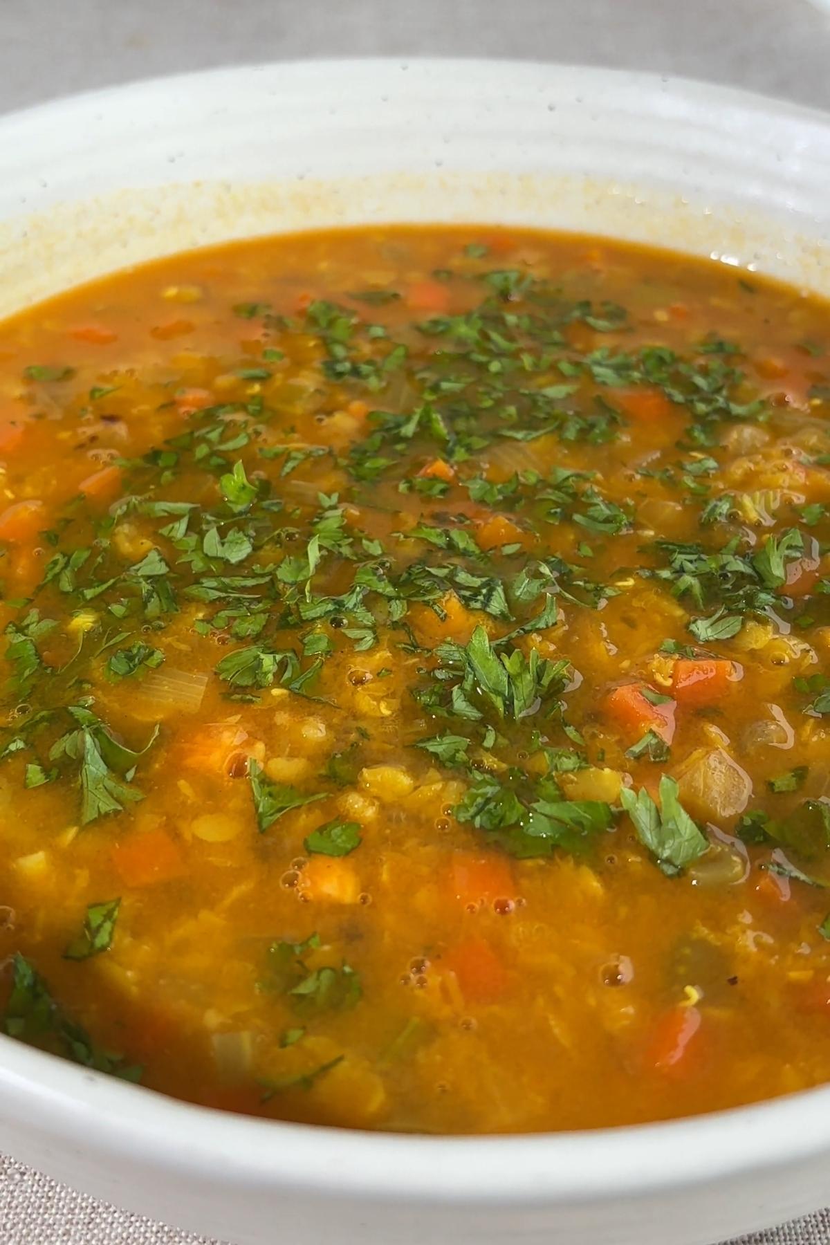 Red lentil coconut soup garnished with chopped cilantro in a white bowl.
