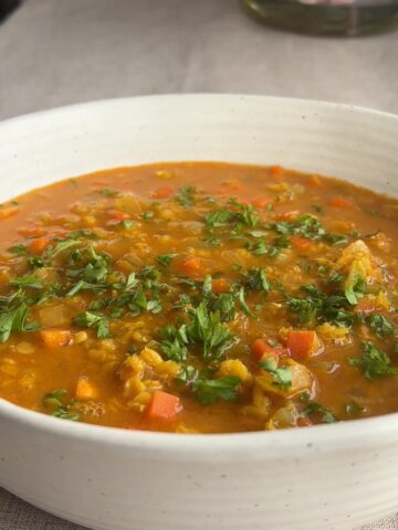 Close-up of red lentil coconut soup garnished with chopped cilantro in a white bowl.