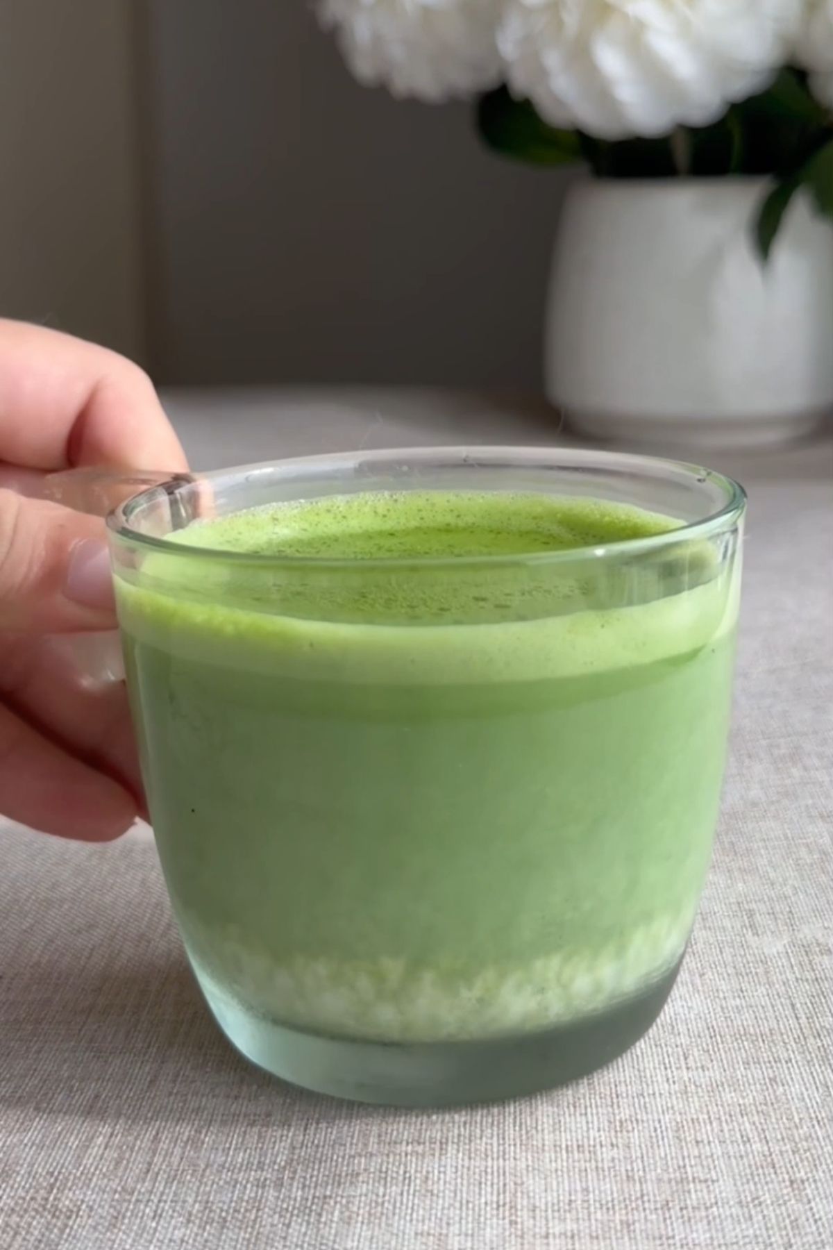 Hot green latte in a clear glass cup.