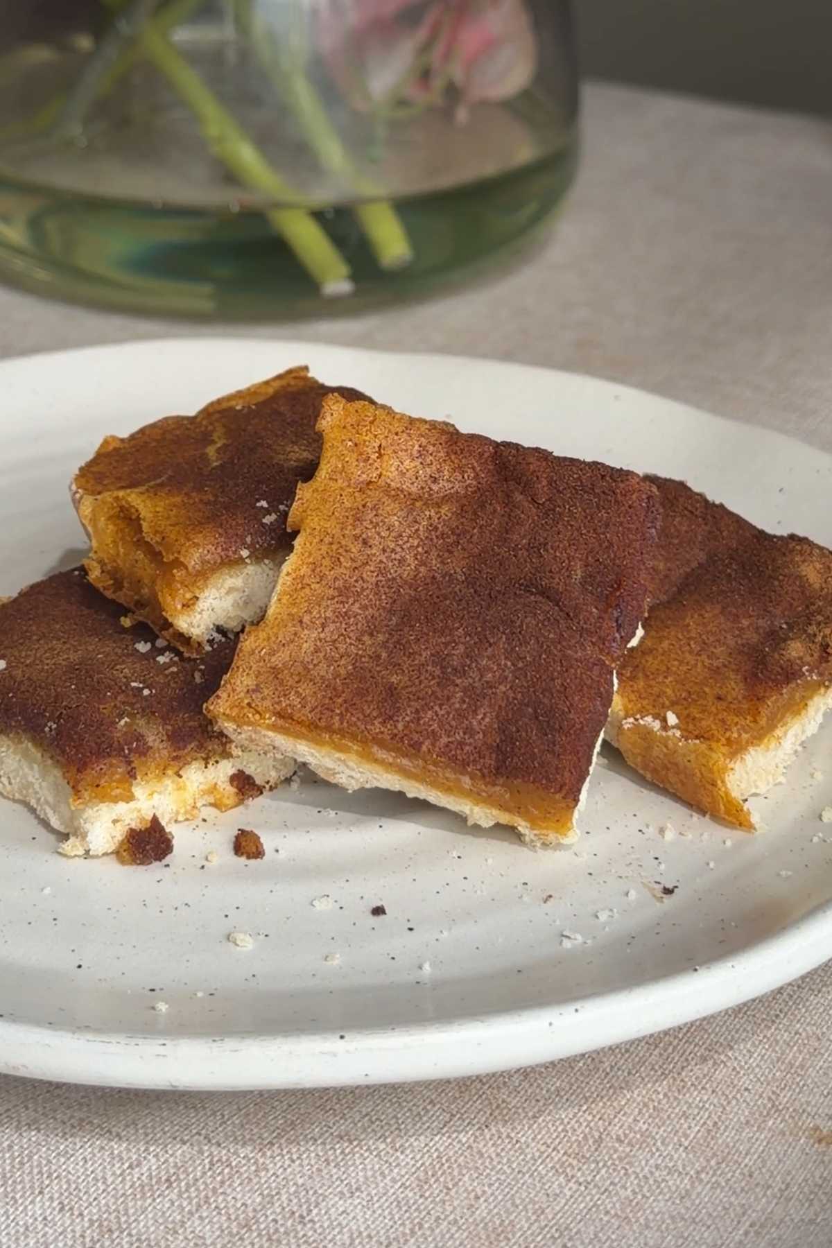 Stack of vegan sweet potato pie bars dusted with cinnamon on a white plate.