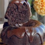 A slice lifted from a chocolate Bundt cake topped with glossy chocolate icing.
