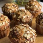 Golden banana muffins topped with rolled oats on a wooden board.