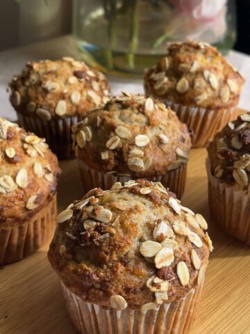 Golden banana muffins topped with rolled oats on a wooden board.