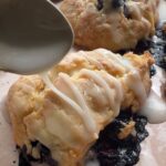 Blueberry scones on a baking tray with glaze drizzled over the tops.