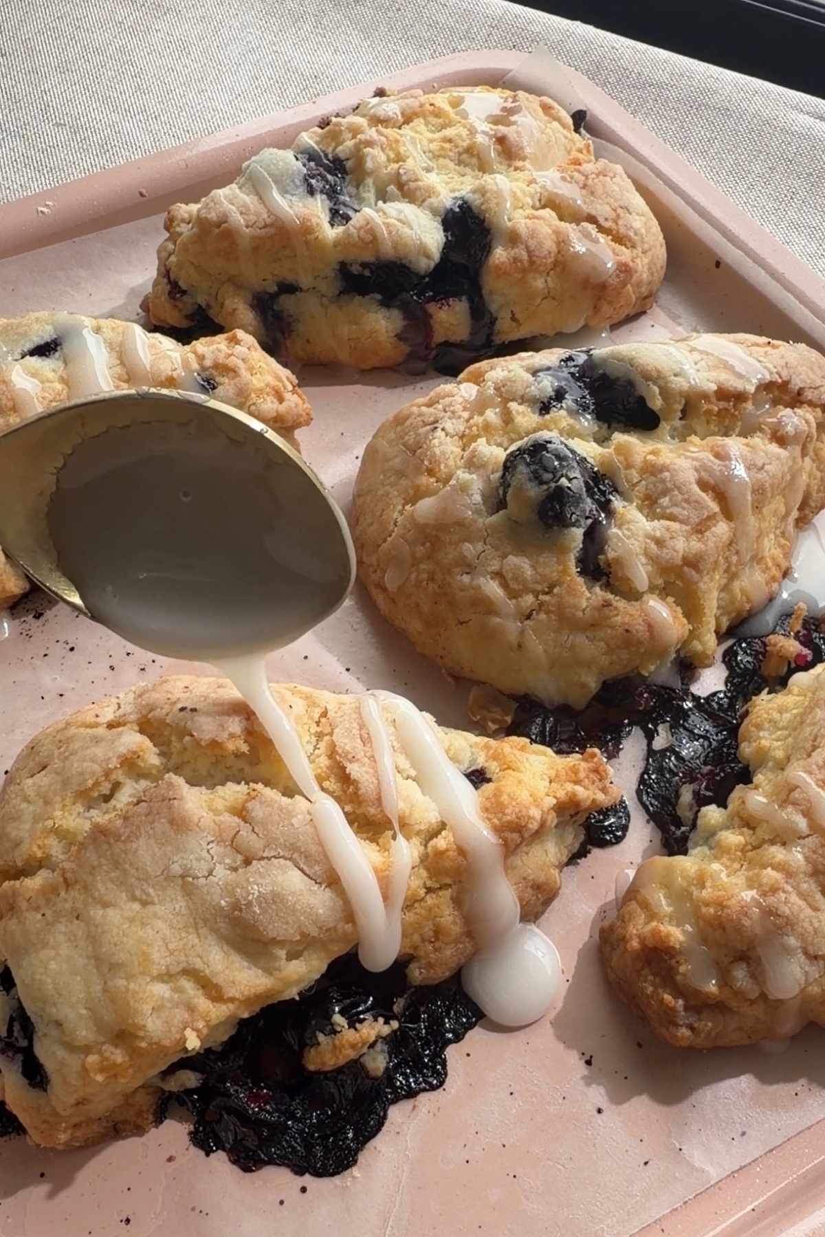 Glaze being drizzled over freshly baked blueberry scones on a baking tray.