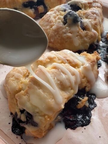 Blueberry scones on a baking tray with glaze drizzled over the tops.