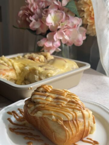 Cinnamon roll on a plate with thick frosting and caramel drizzle.