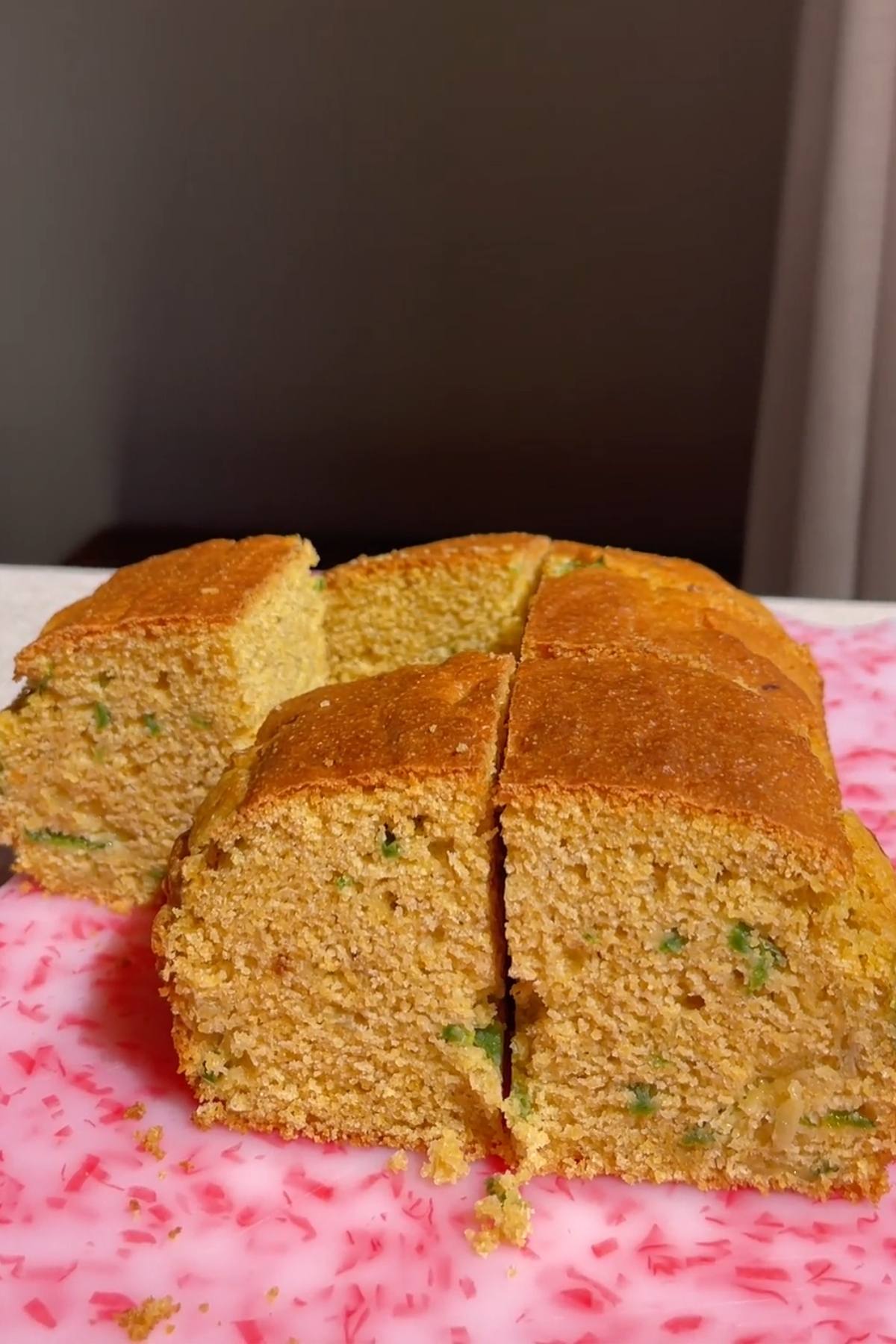 Square vegan jalapeño cornbread cut into six pieces on a pink cutting board.