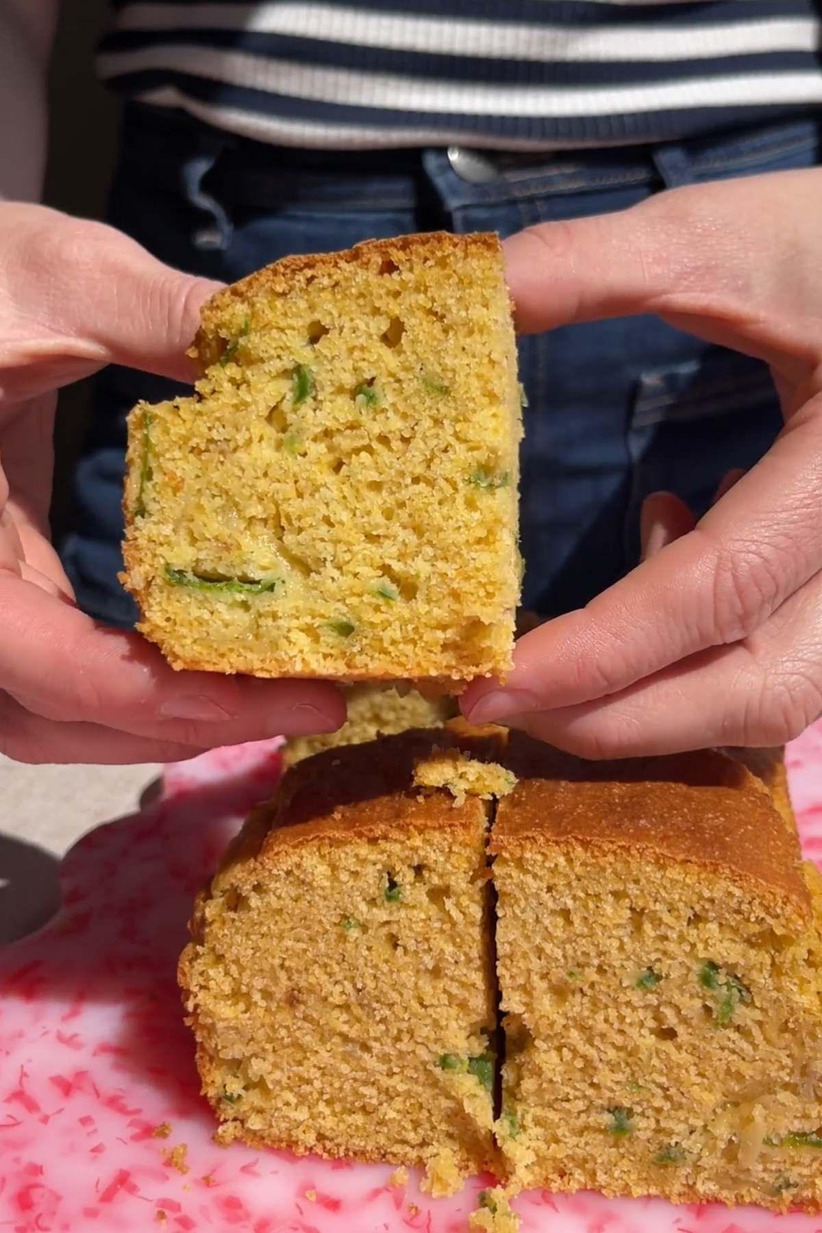 Hands holding a slice of vegan jalapeño cornbread above the remaining cut pieces.