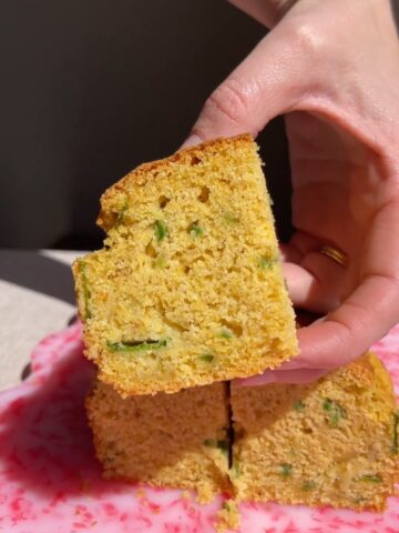 Square slice of vegan jalapeño cornbread held up to show the soft, tender interior.