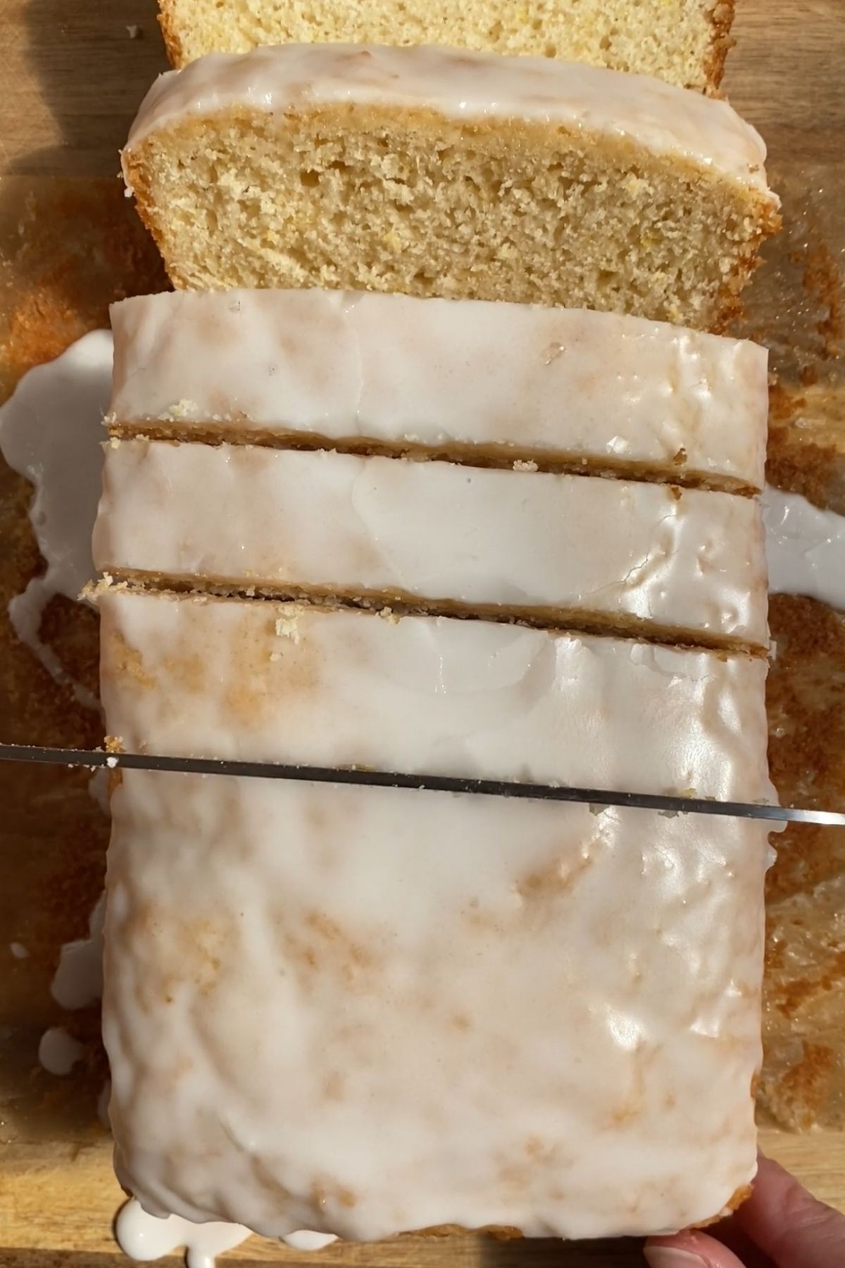 Glazed vegan lemon loaf being sliced on a wooden board.
