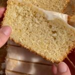 Slice of glazed vegan lemon loaf held up to show the soft, fluffy crumb.