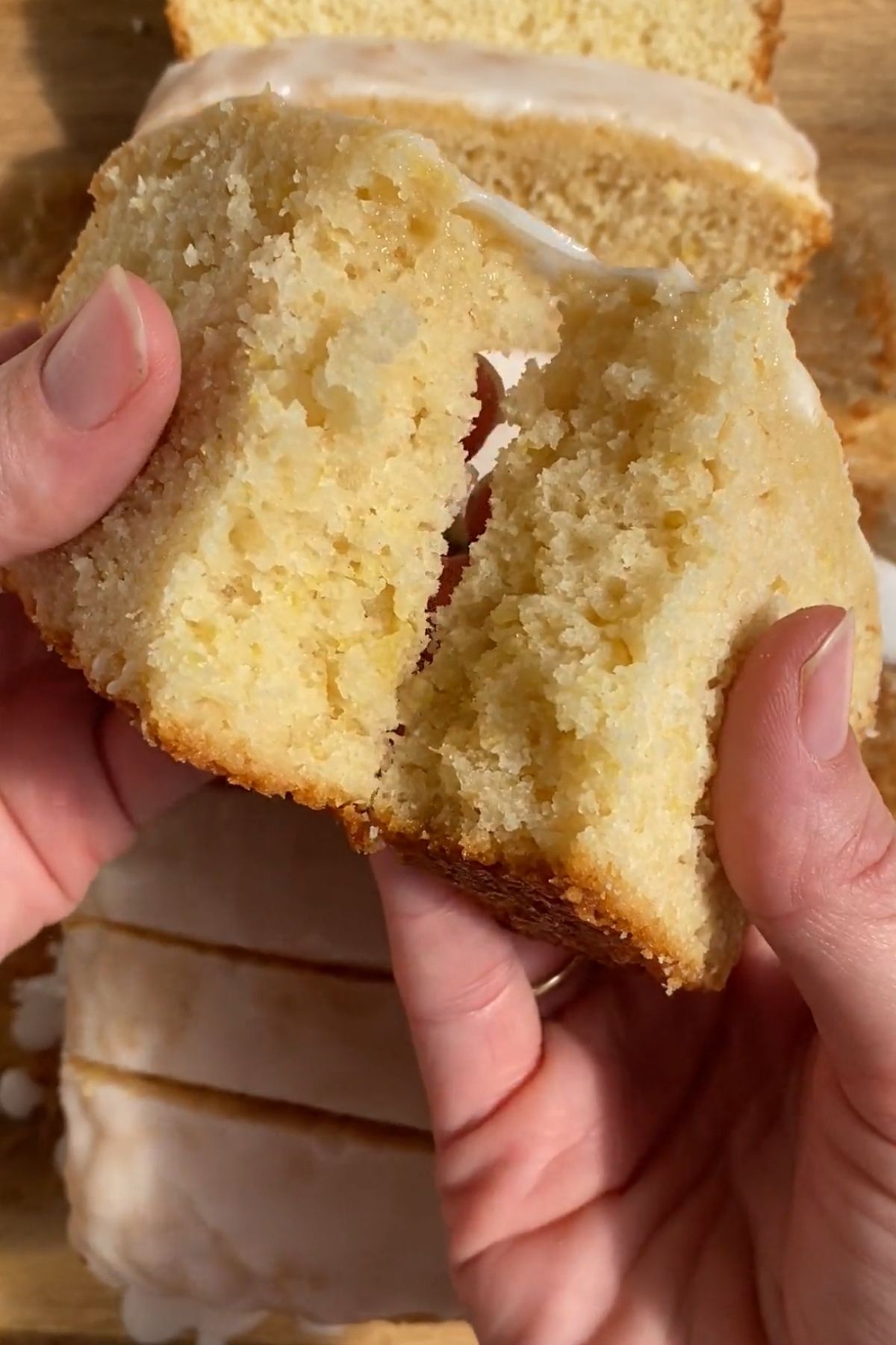 Hands pulling apart a slice of glazed vegan lemon loaf.