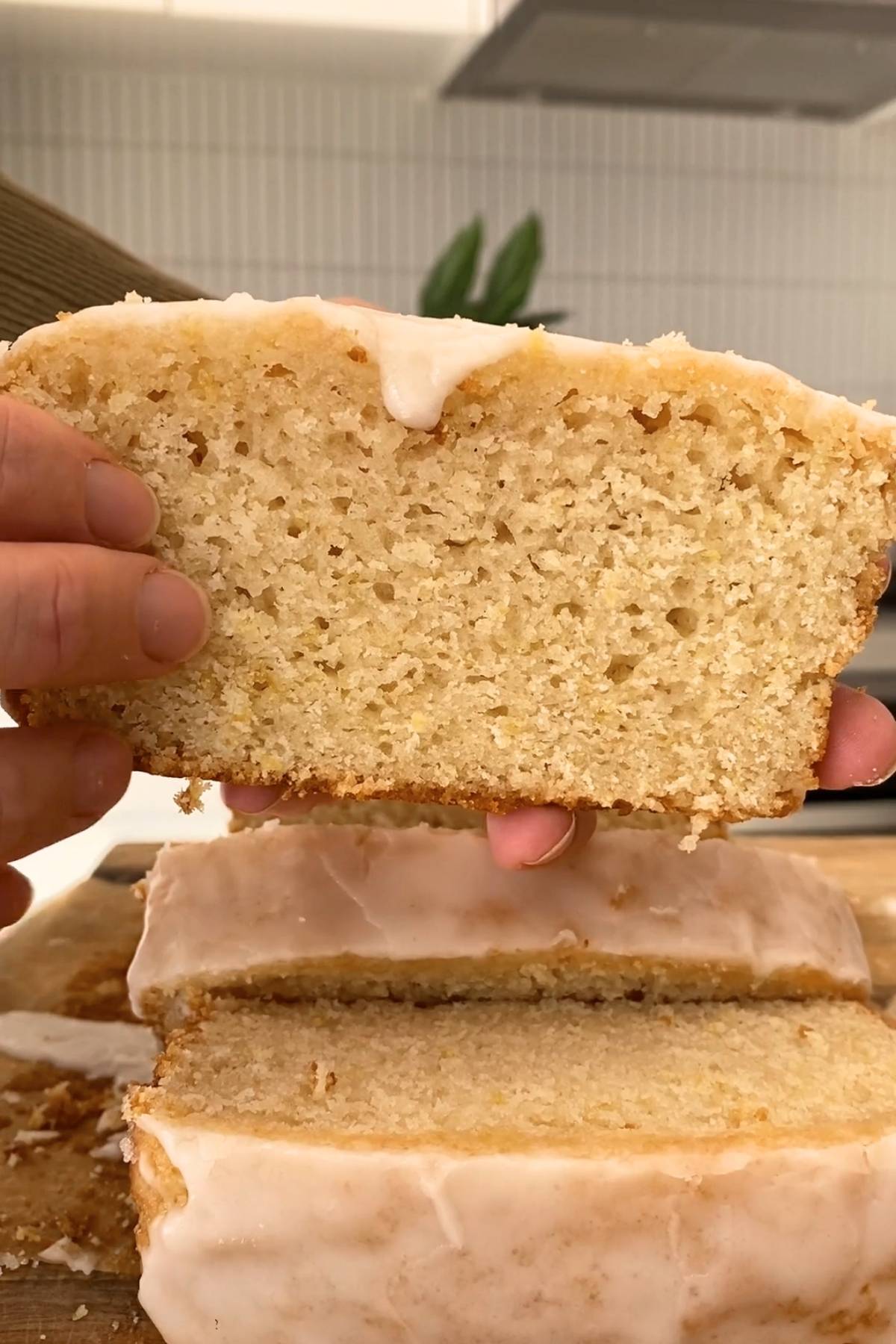 Glazed vegan lemon loaf with a slice lifted to show the soft, tender crumb.