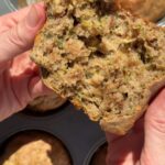 Hands holding a fluffy vegan zucchini muffin with a moist crumb and shredded zucchini visible.