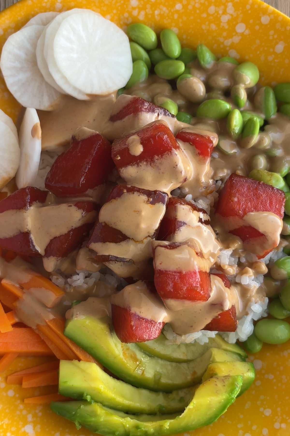 Watermelon poke bowl with creamy sauce over watermelon, rice, edamame, avocado, and carrots.