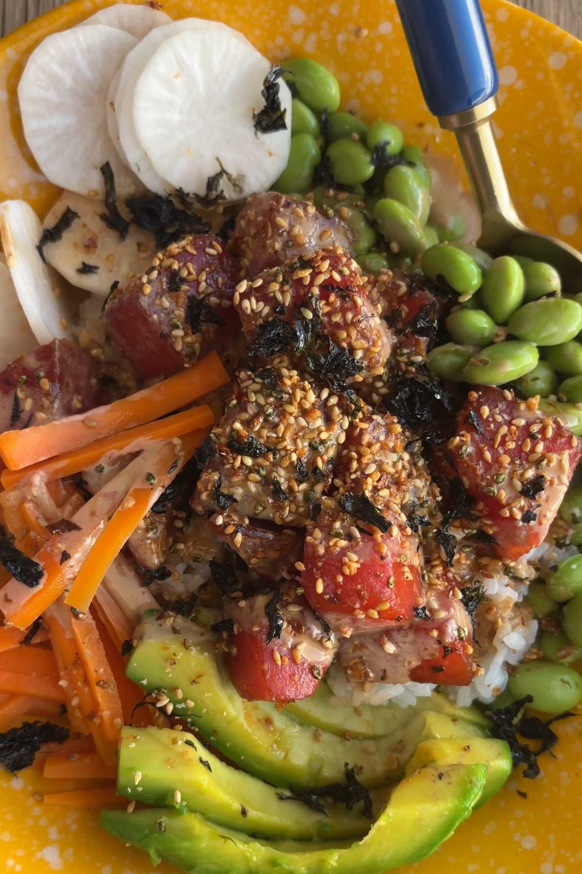 Spoon scooping a bite from a watermelon poke bowl with avocado and edamame.