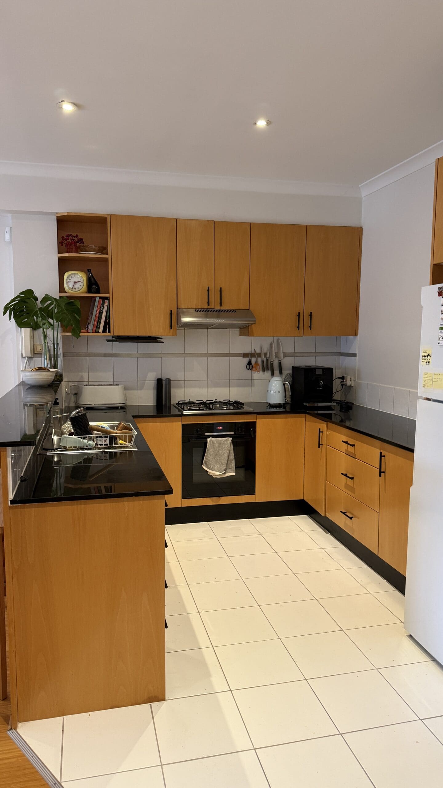 Kitchen with black benchtops, yellow wood cabinetry and white tiles.