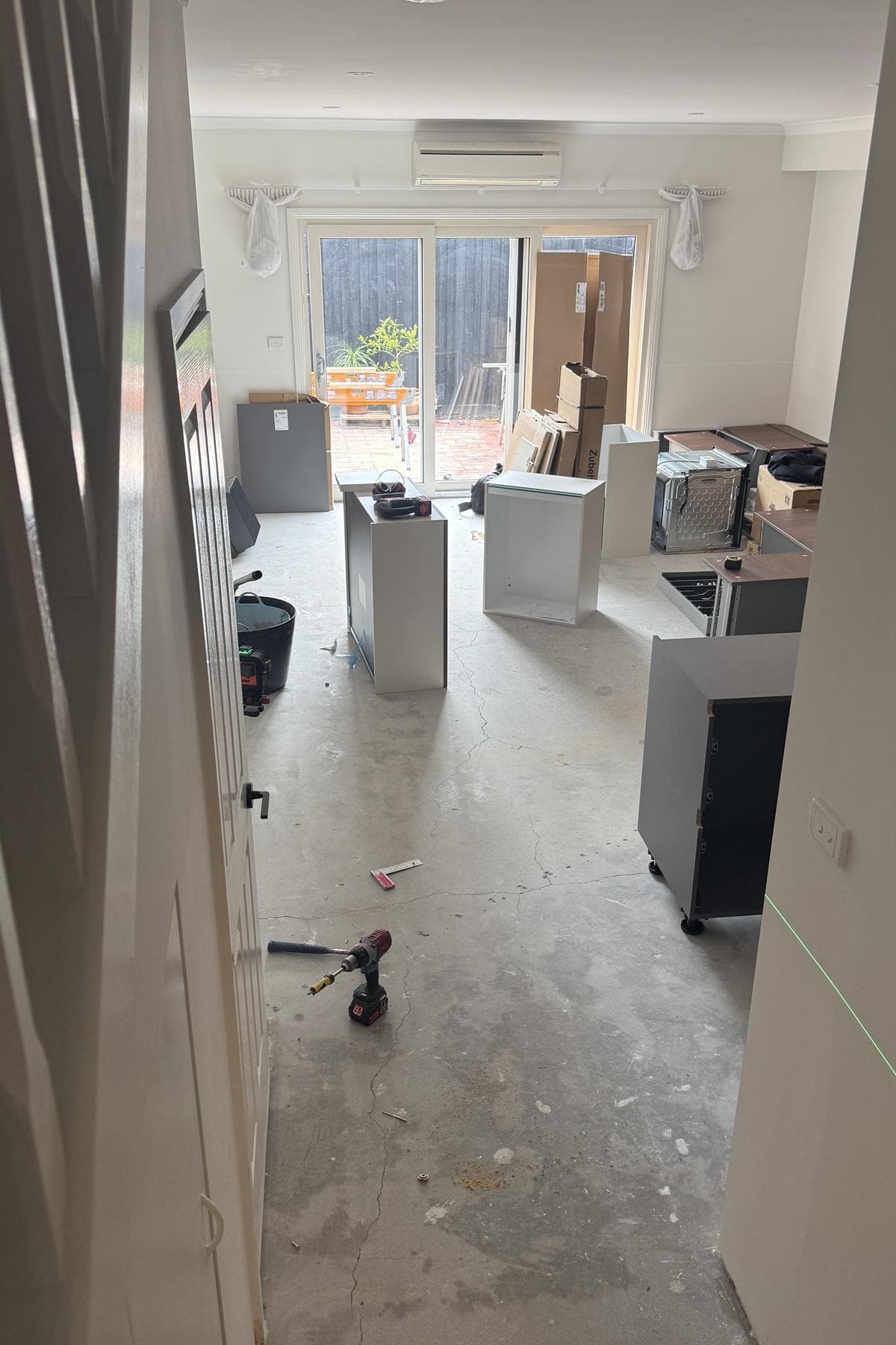 Room filled with cabinet panels, boxes and tools on a bare concrete floor.