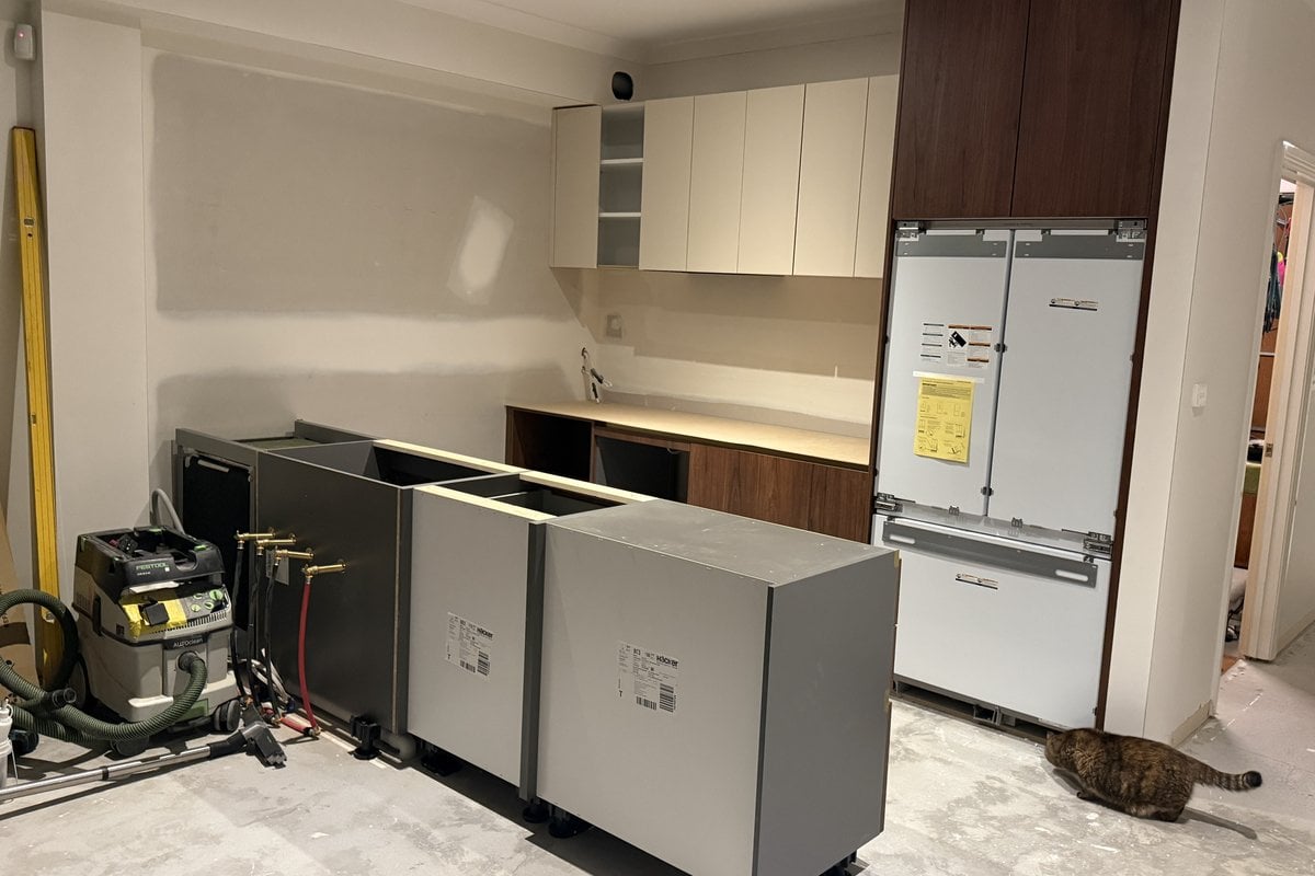 Integrated fridge fitted inside tall walnut cabinetry beside cream upper cabinets.
