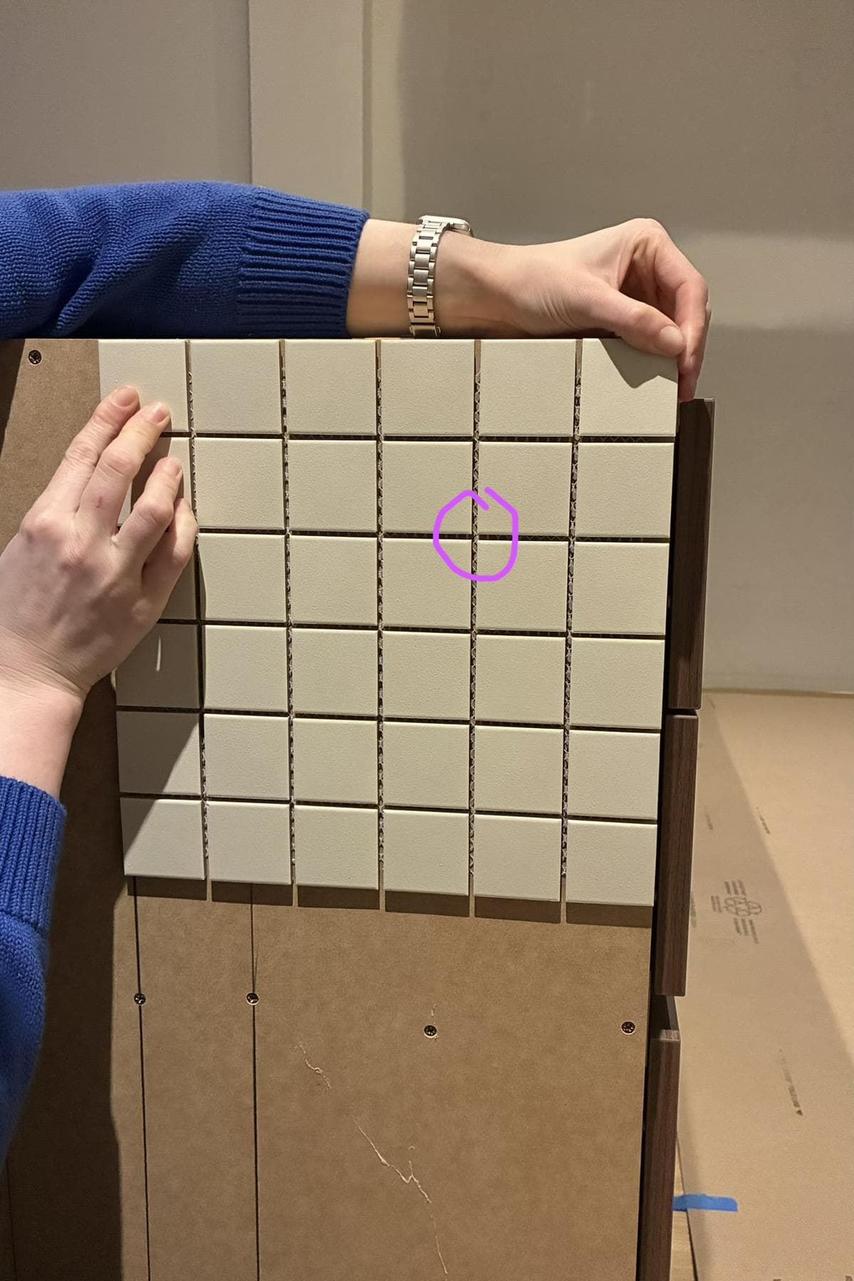 Hands holding a sheet of square bone tiles against a raw curved island.