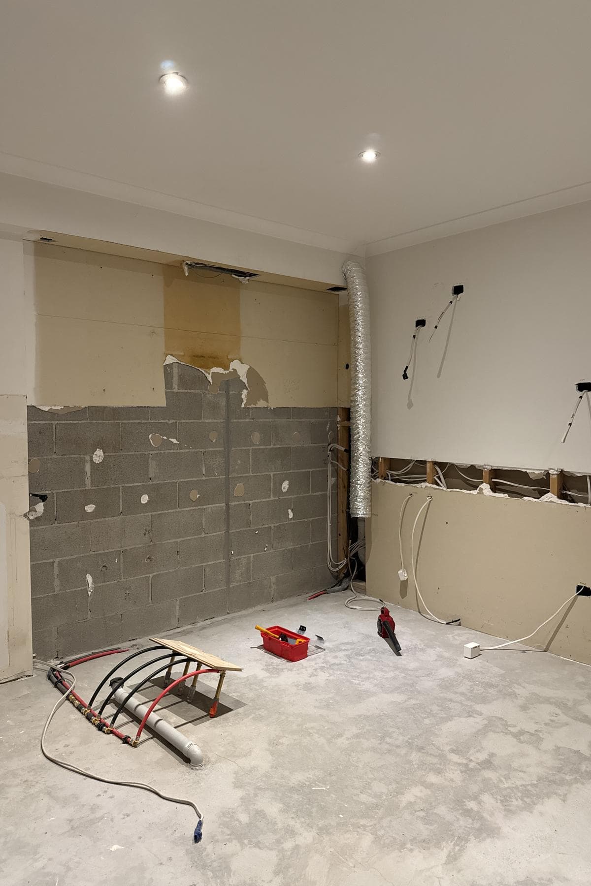New pipework across a concrete slab with ducting and electrical cables in a stripped wall.