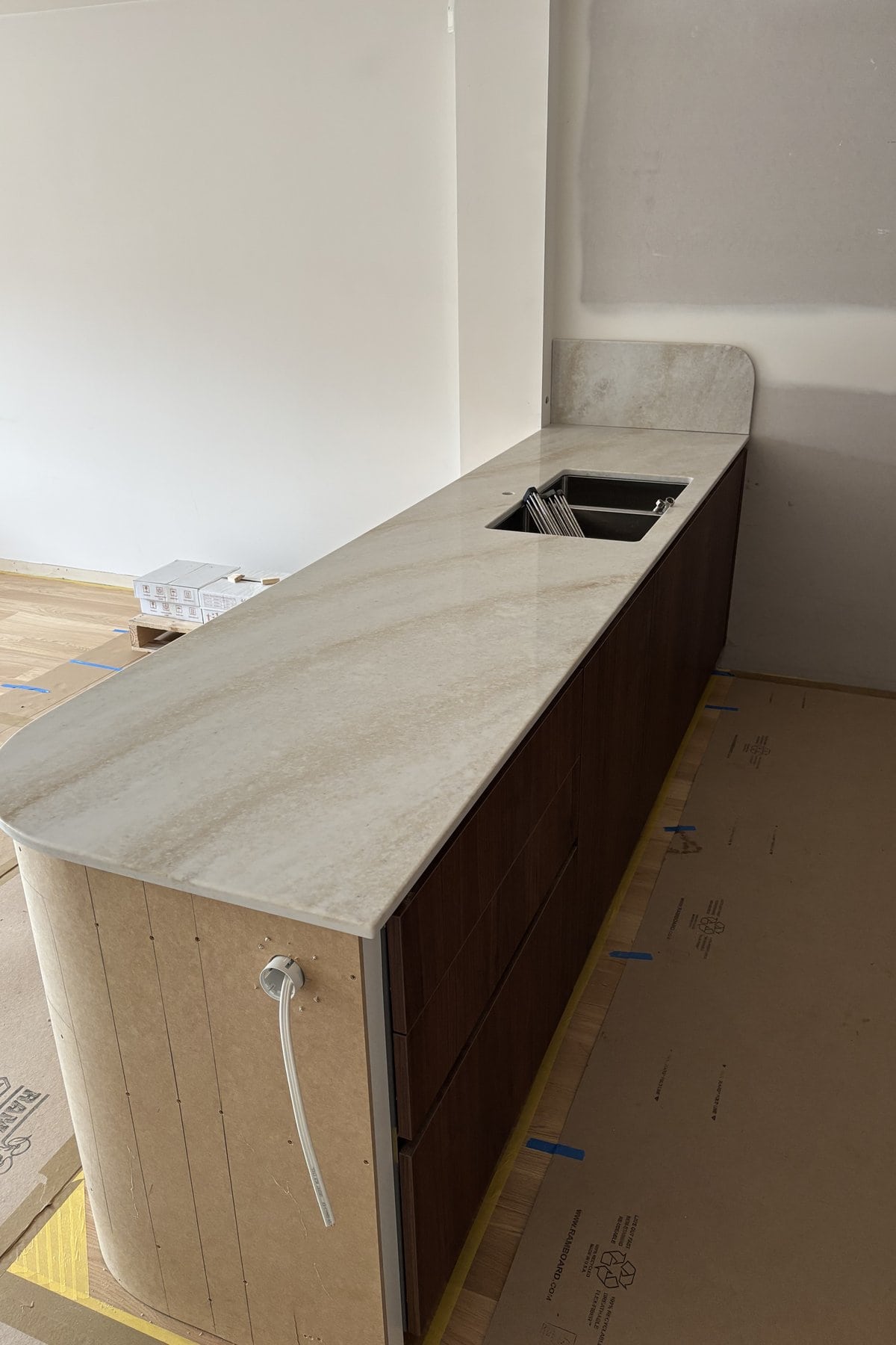 Stone island benchtop with a curved end, an undermount sink and walnut drawers below.