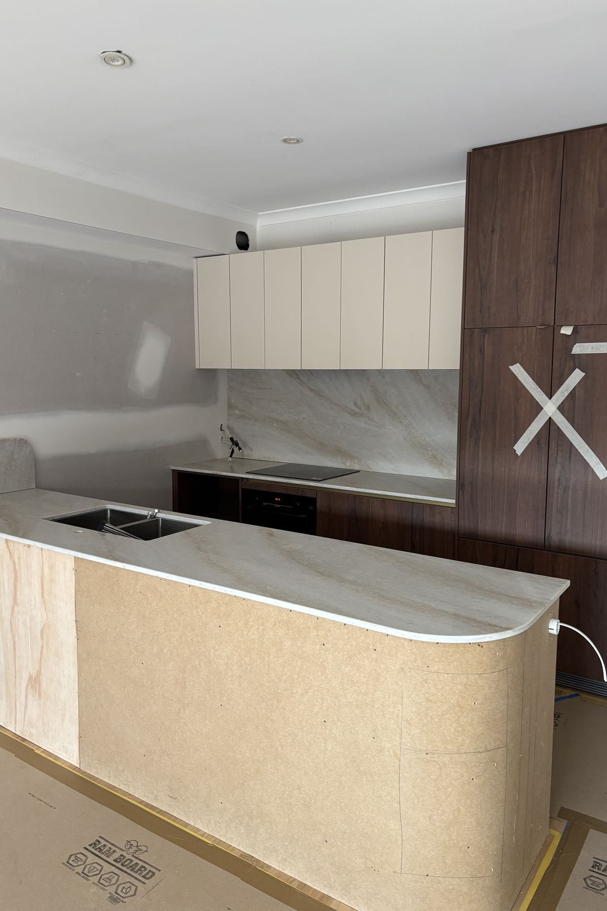 Stone benchtop and full height stone splashback behind an induction cooktop.