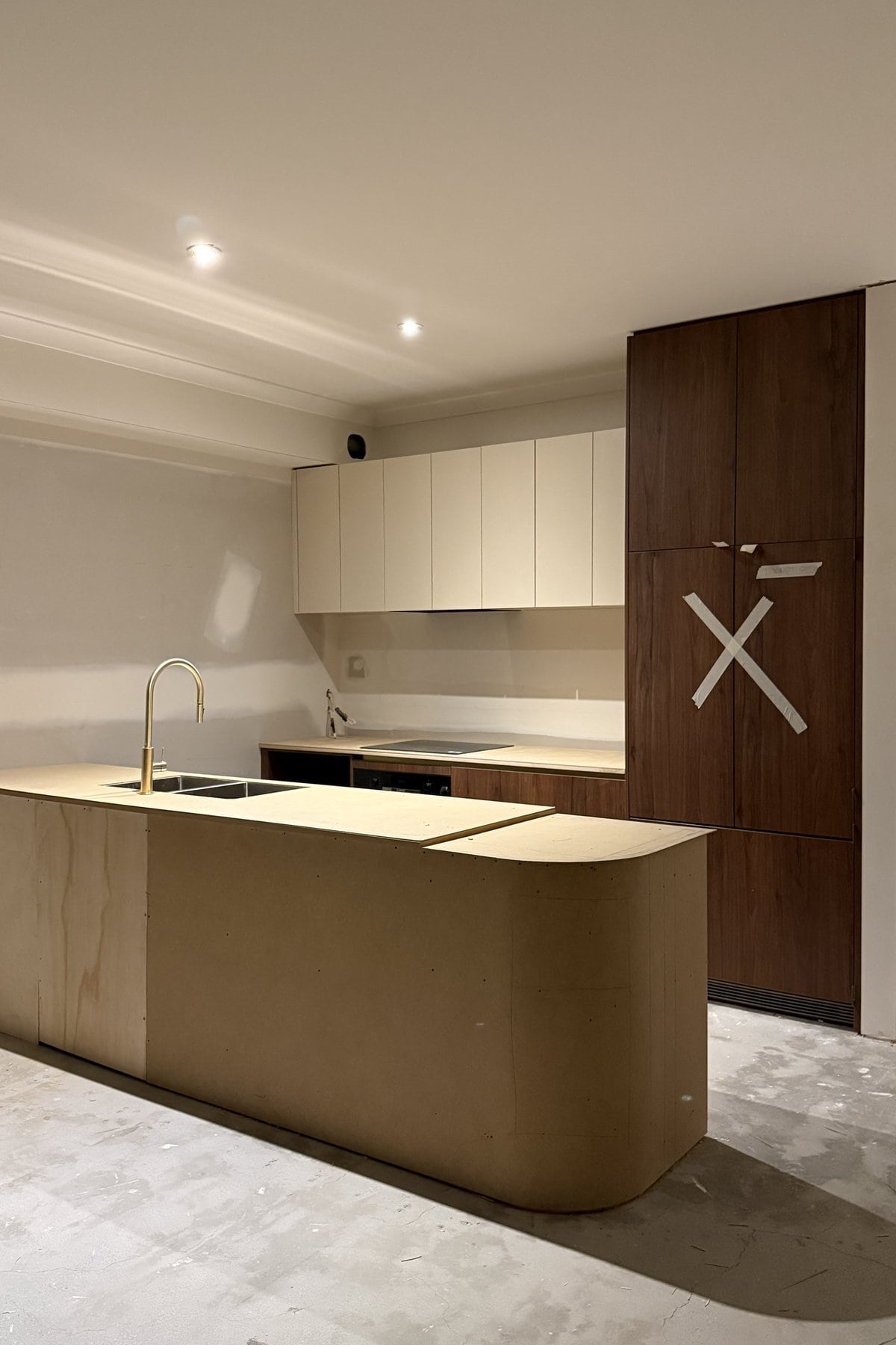 Temporary board benchtops with a gold gooseneck tap and an induction cooktop installed.