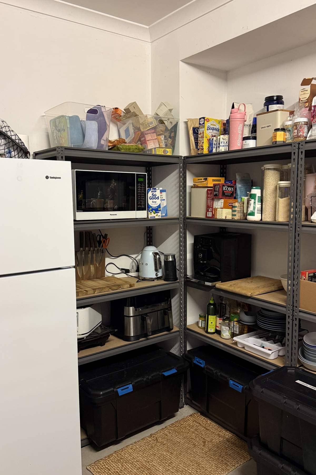 Temporary kitchen on metal shelving with a microwave, kettle, air fryer and small fridge.